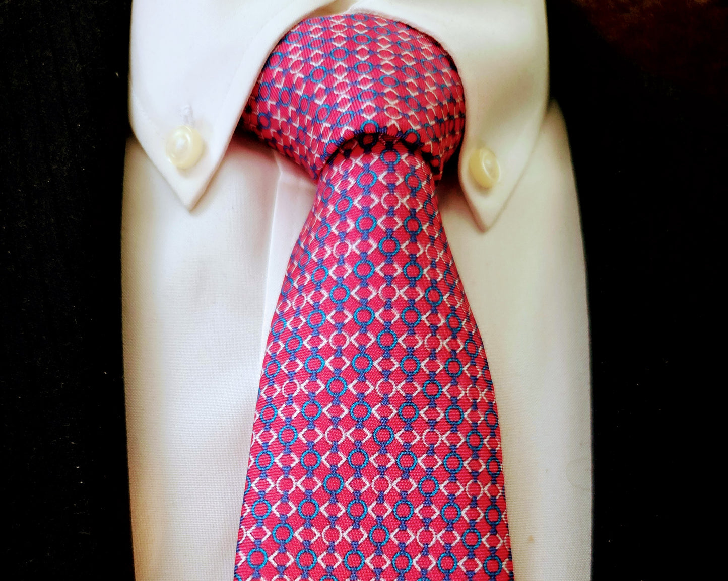 A red and blue patterned necktie knotted on a white dress shirt, displayed against a black background.
