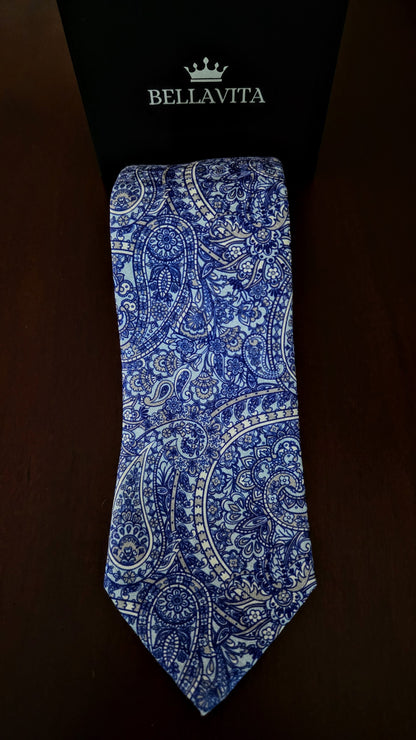 A blue and white paisley pattern necktie displayed vertically against a black Bellavita box on a dark brown background.