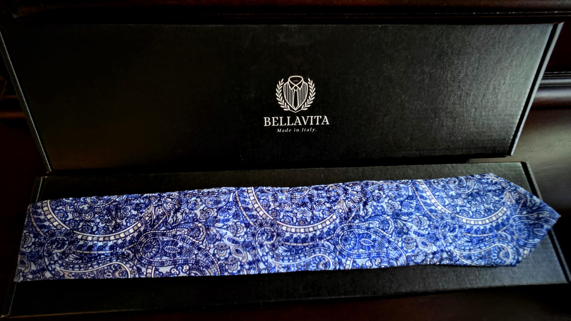 A blue and white paisley pattern necktie displayed inside an open black Bellavita gift box.