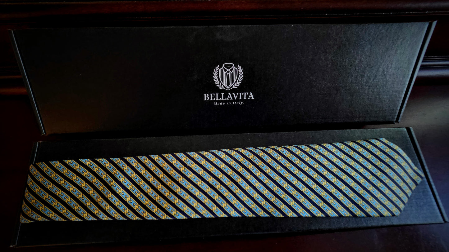 A Bellavita necktie with a blue, yellow, and gold geometric pattern, presented inside an open black gift box with the brand logo visible on the inner lid.