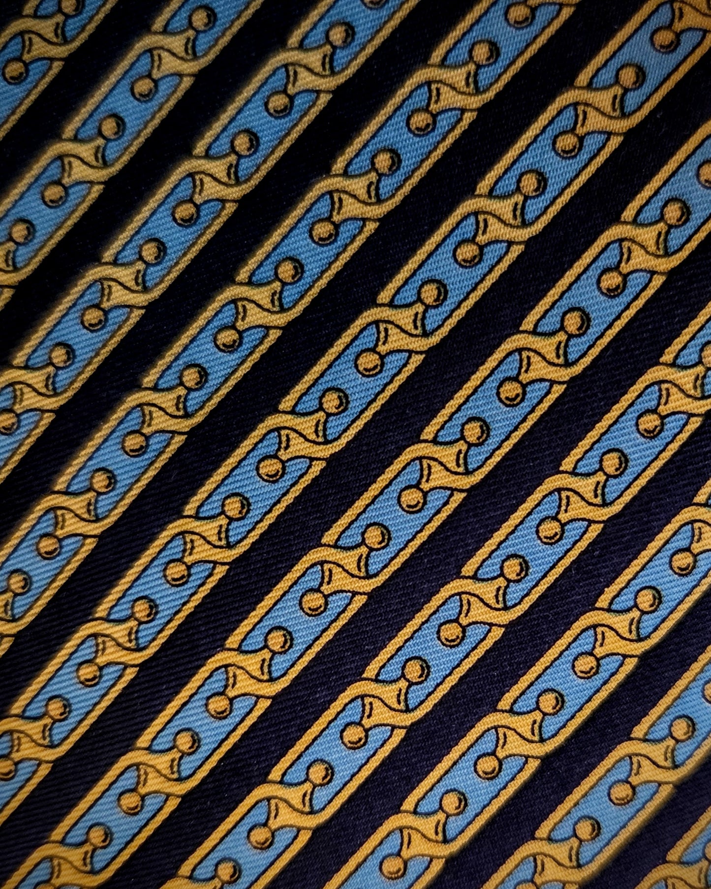 A close-up of a patterned necktie fabric with diagonal stripes of light blue, mustard yellow, and black.
