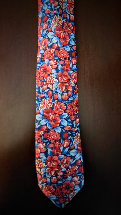 A necktie with a vibrant red and blue floral pattern, laid flat against a dark brown background.