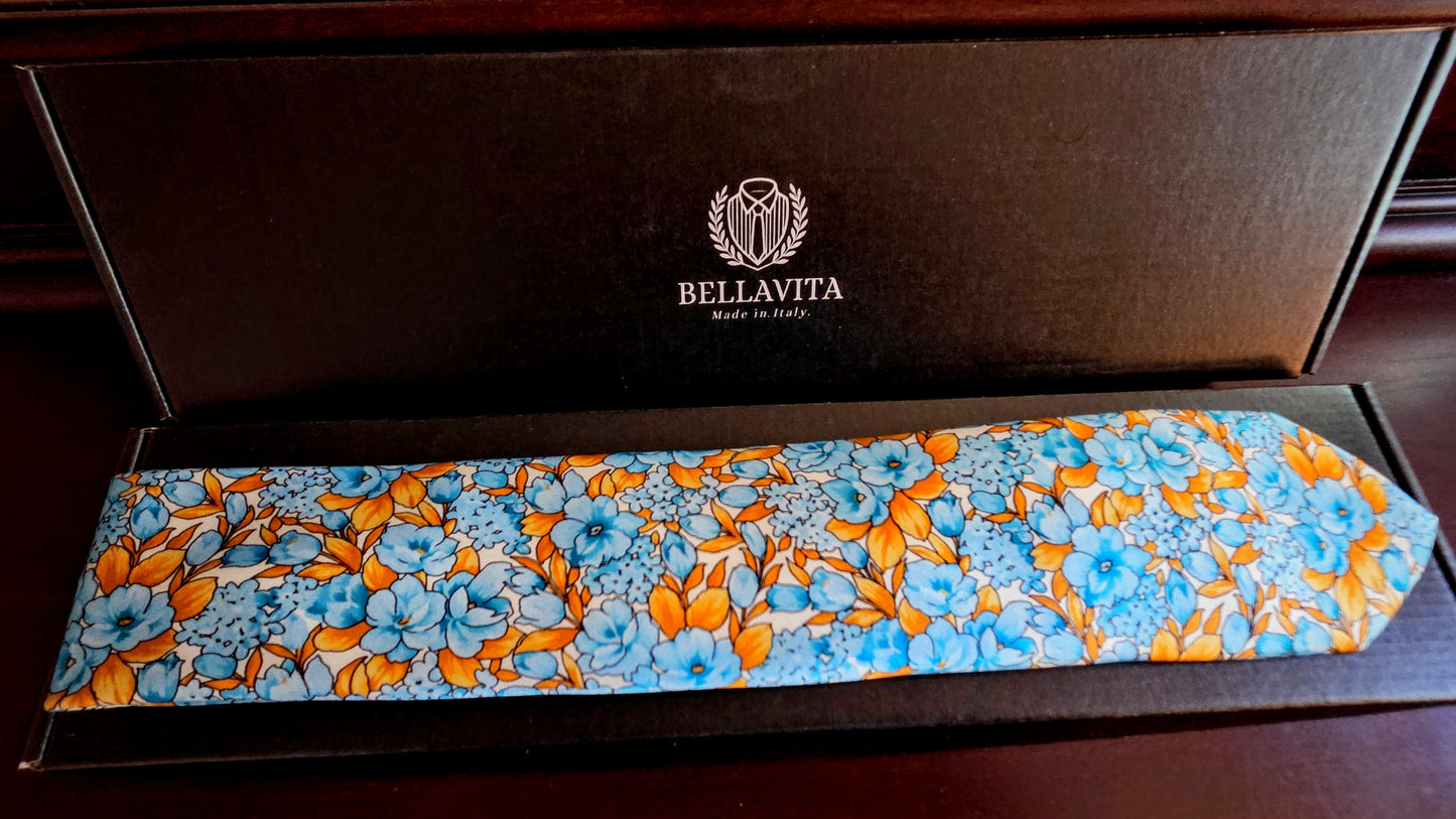 A Bellavita silk necktie with a vibrant blue and orange floral pattern, presented inside its dark brown branded gift box.