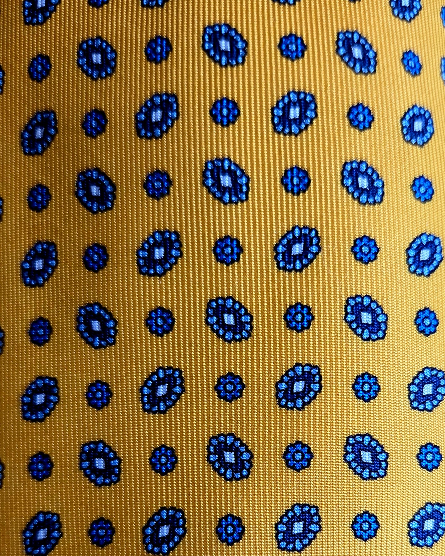 A close-up of a woven fabric with a mustard yellow background and a repeating pattern of blue circular medallions and dots.