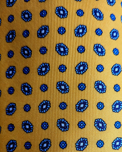 A close-up of a woven fabric with a mustard yellow background and a repeating pattern of blue circular medallions and dots.