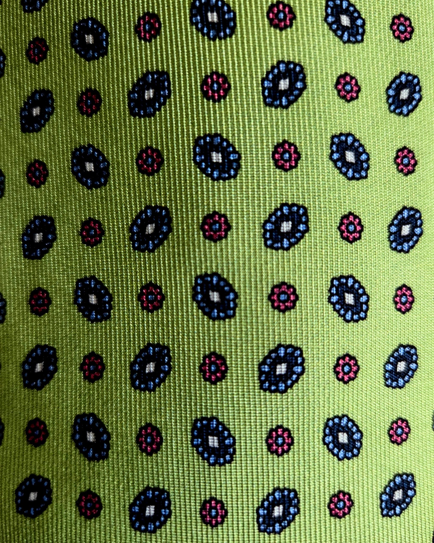A close-up of a woven fabric with a repeating geometric pattern on a bright lime green background, featuring dark blue, pink, and black motifs.