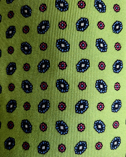 A close-up of a woven fabric with a repeating geometric pattern on a bright lime green background, featuring dark blue, pink, and black motifs.