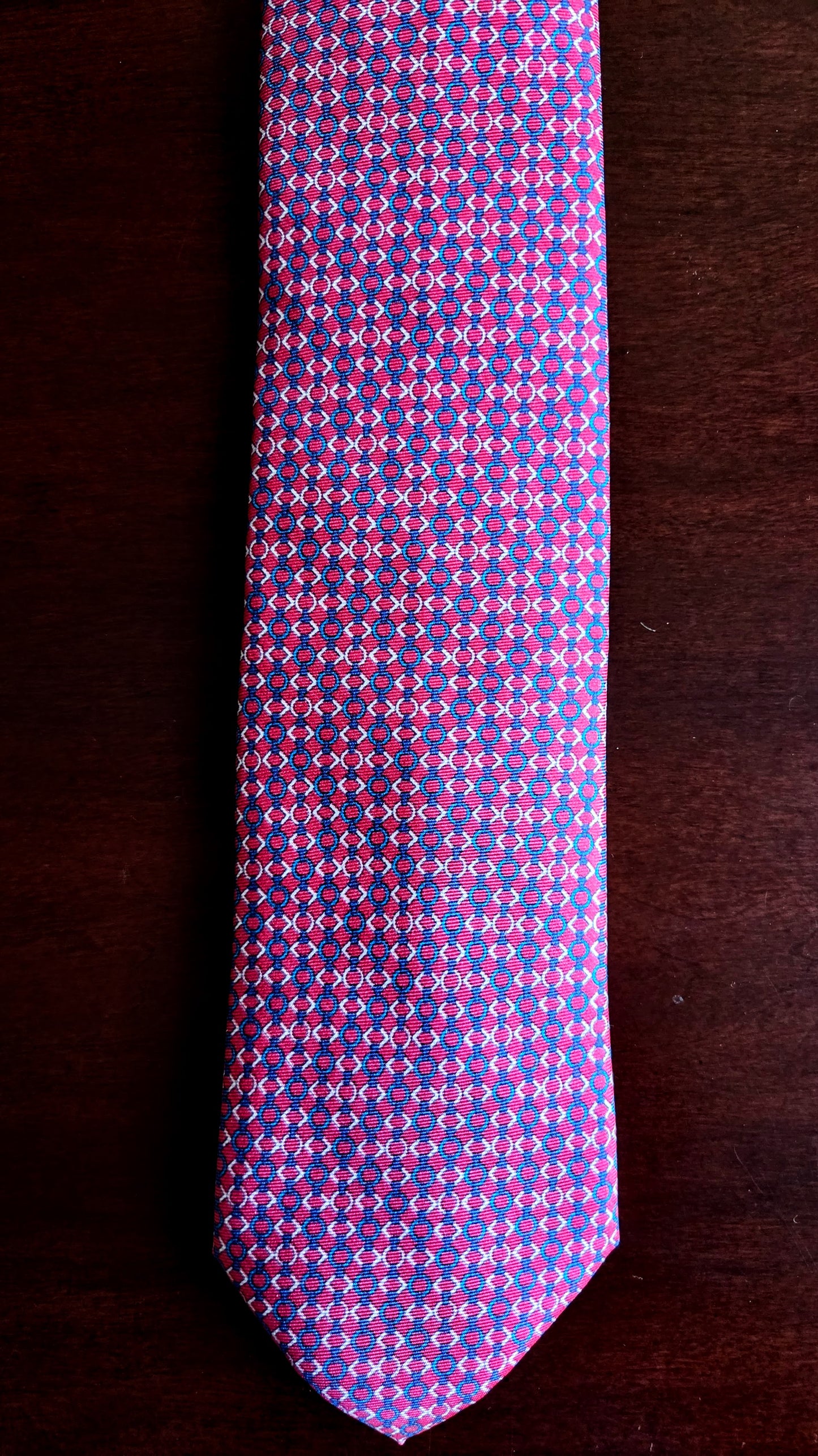 A purple and pink patterned necktie laid flat on a dark brown wooden surface.