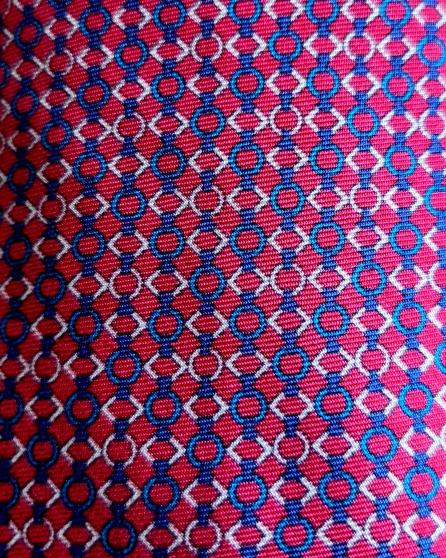 A close-up of a woven fabric pattern featuring a red background with repeating blue and white interlocking circle-and-diamond motifs.