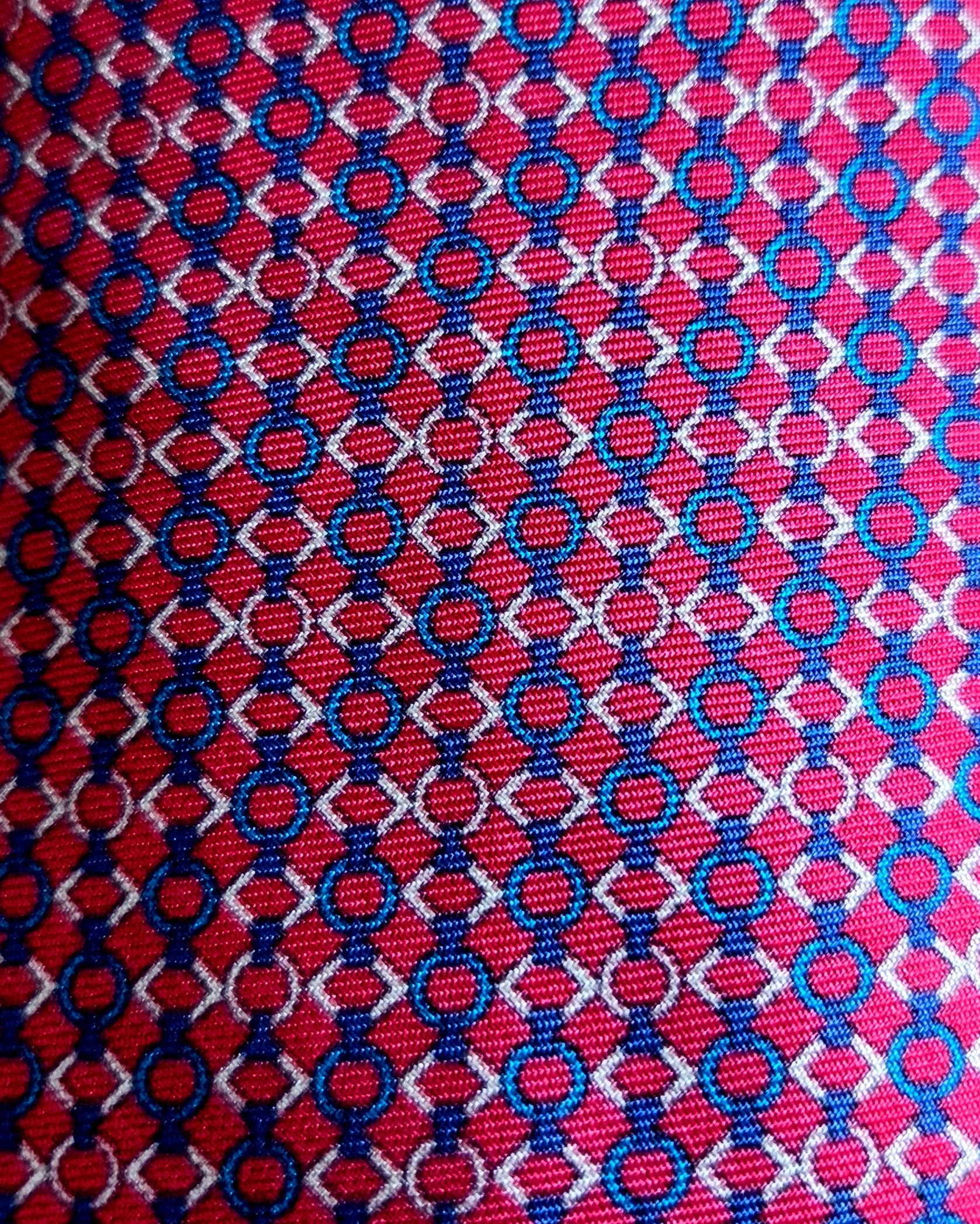 A close-up of a woven fabric pattern featuring a red background with repeating blue and white interlocking circle-and-diamond motifs.