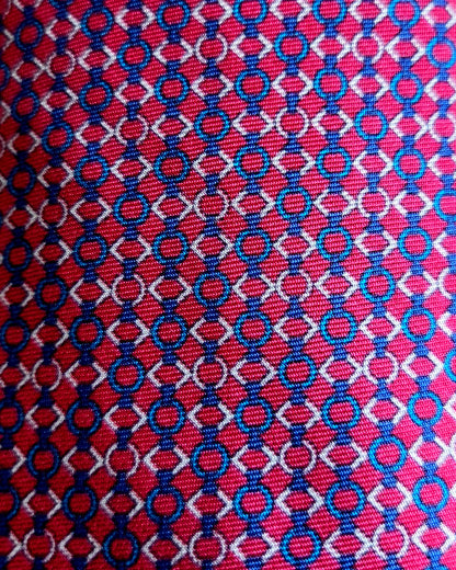 A close-up of a woven fabric pattern featuring a red background with repeating blue and white interlocking circle-and-diamond motifs.