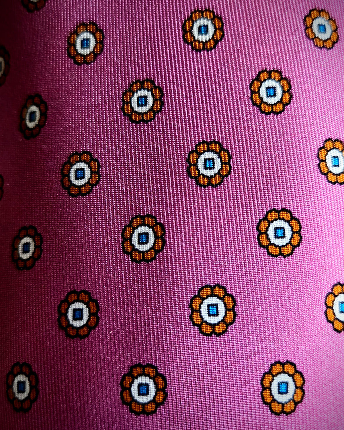 A close-up of a pink woven fabric with a repeating circular floral pattern in orange, white, and blue.