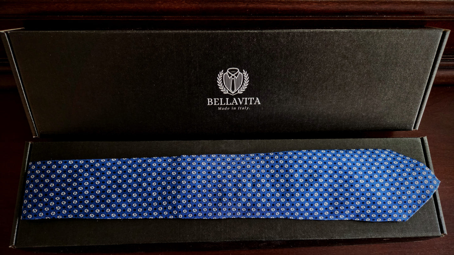 A blue necktie with a small white geometric pattern, presented inside an open black Bellavita gift box on a dark wooden surface.