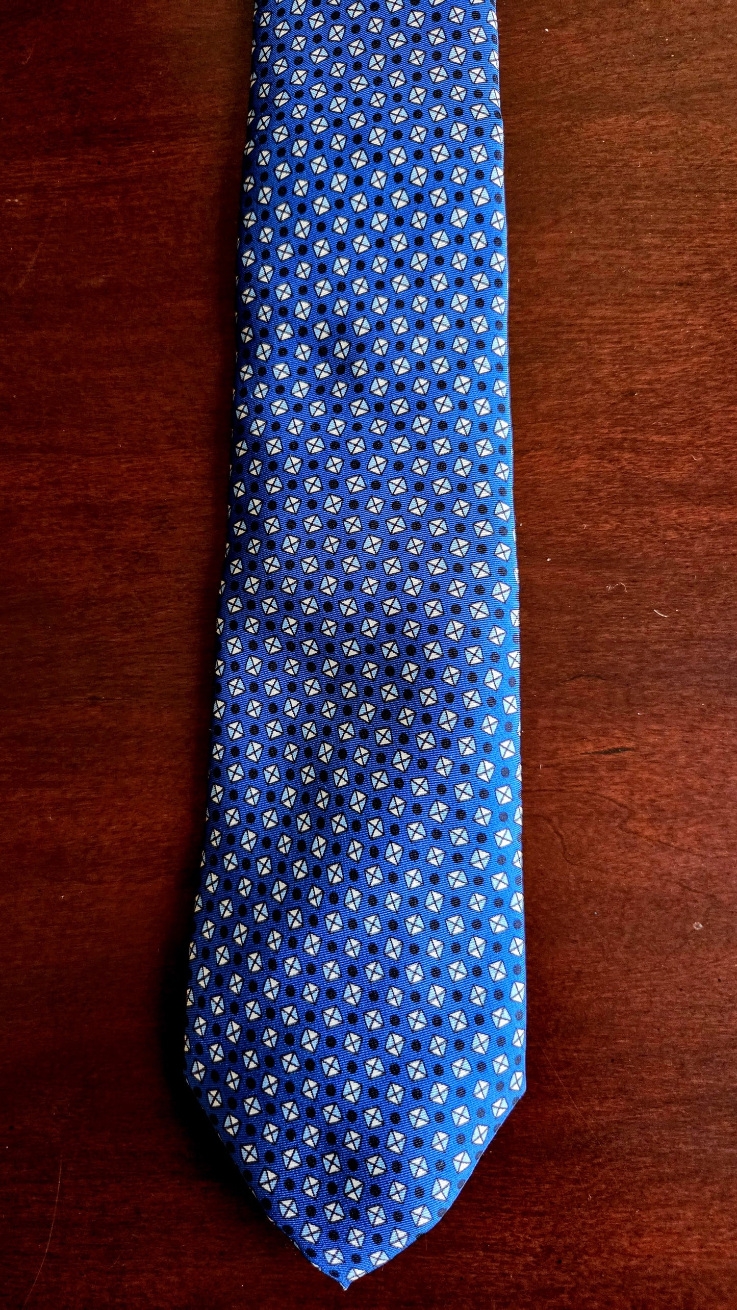 A blue necktie with a repeating white and light blue floral pattern, laid flat on a dark brown wooden surface.