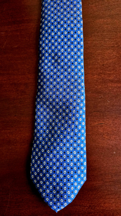 A blue necktie with a repeating white and light blue floral pattern, laid flat on a dark brown wooden surface.
