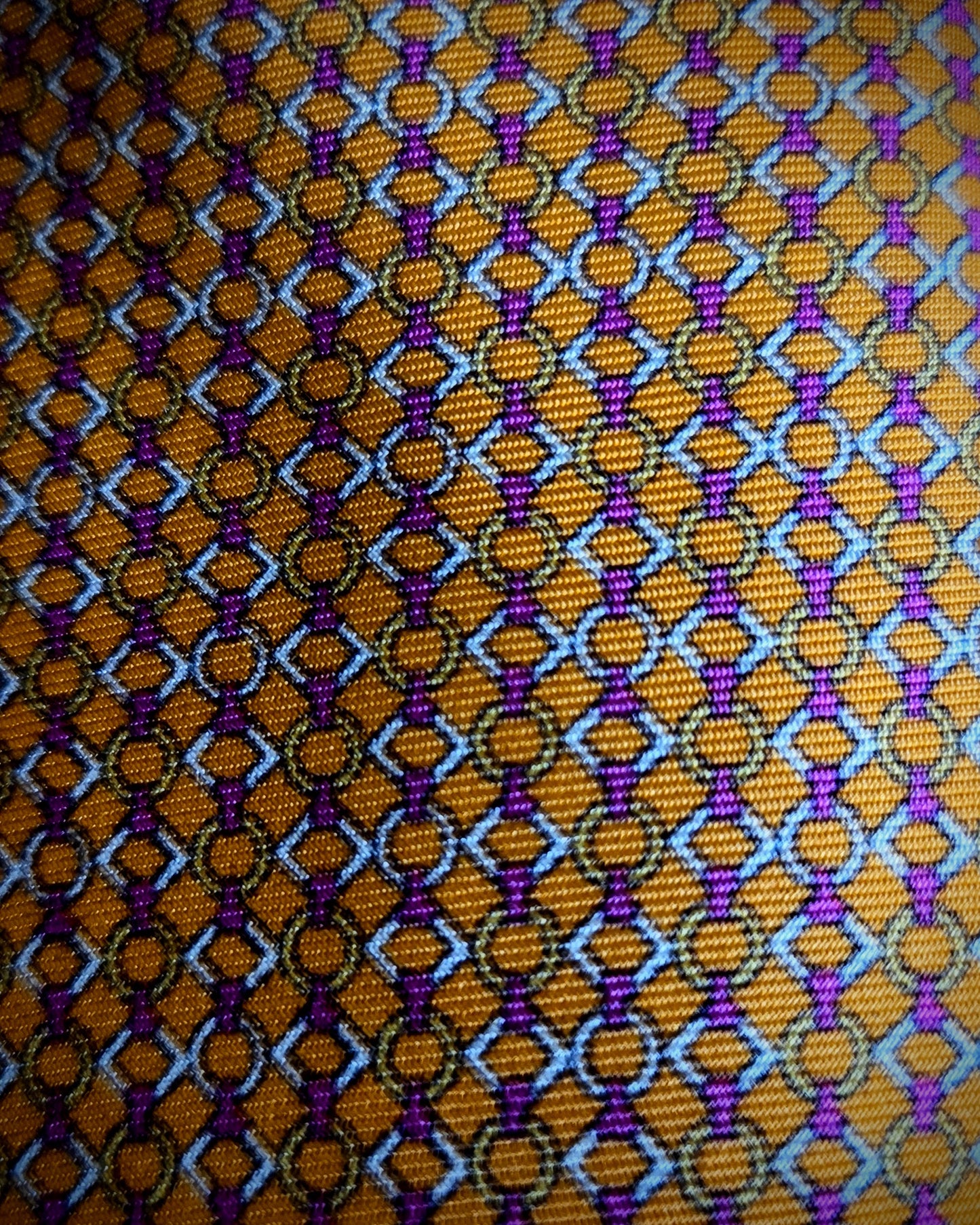 A close-up of a woven fabric pattern featuring a repeating geometric design in orange, purple, light blue, and black.