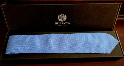 A light blue textured necktie presented inside an open black Bellavita gift box on a dark wooden surface.