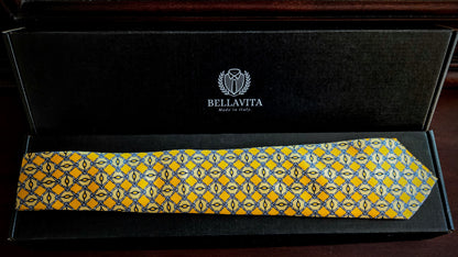 A yellow patterned silk necktie with a geometric design, presented inside an open black Bellavita gift box.