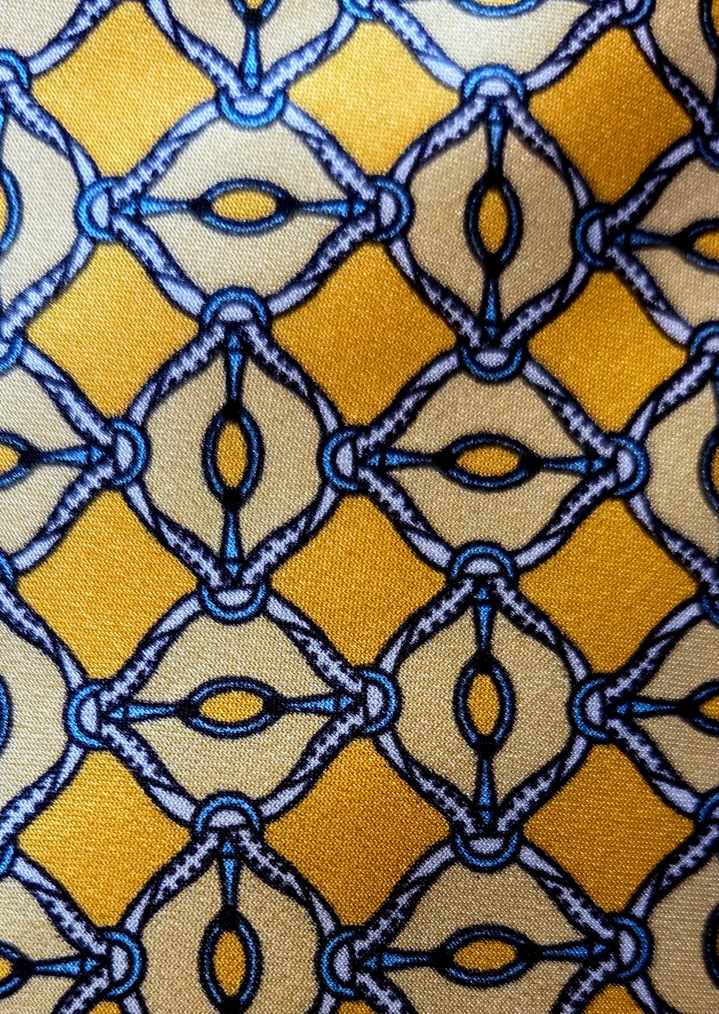 A close-up of a patterned fabric featuring a repeating geometric design with mustard yellow, beige, and blue interlocking diamond and oval motifs.