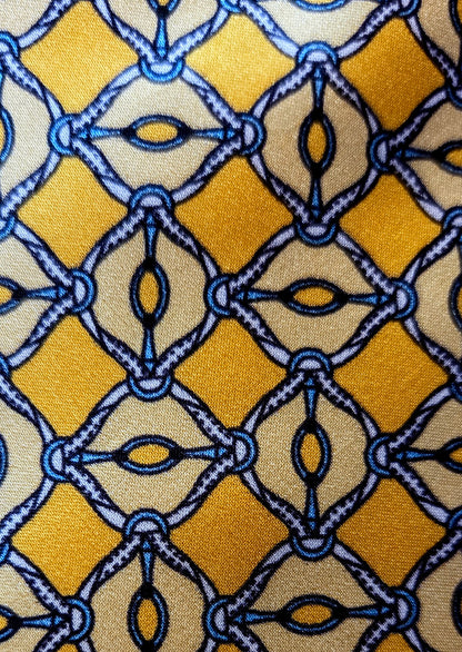 A close-up of a patterned fabric featuring a repeating geometric design with mustard yellow, beige, and blue interlocking diamond and oval motifs.