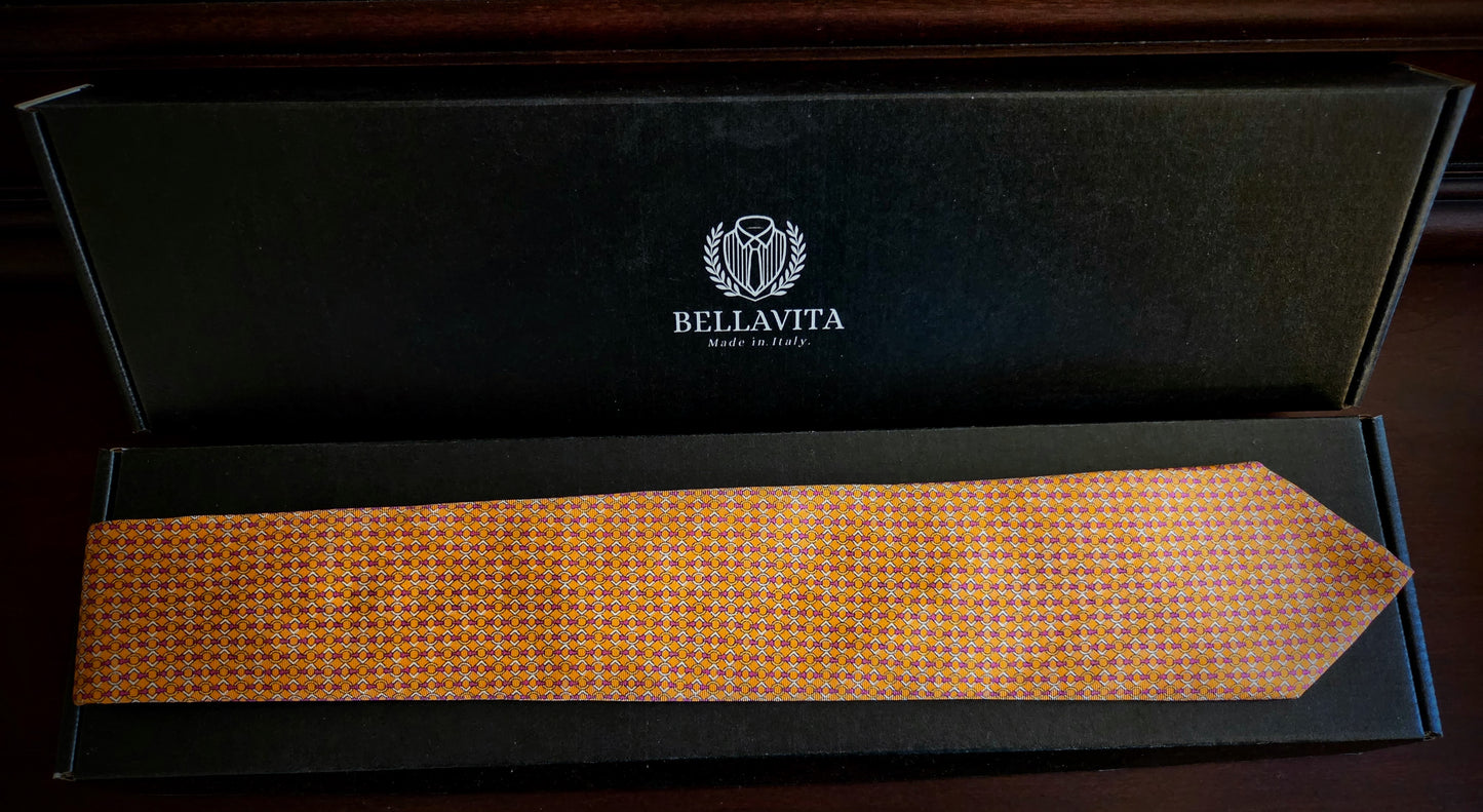 A Bellavita silk necktie with a gold and orange geometric pattern, presented inside an open black gift box with the brand logo visible on the inside lid.