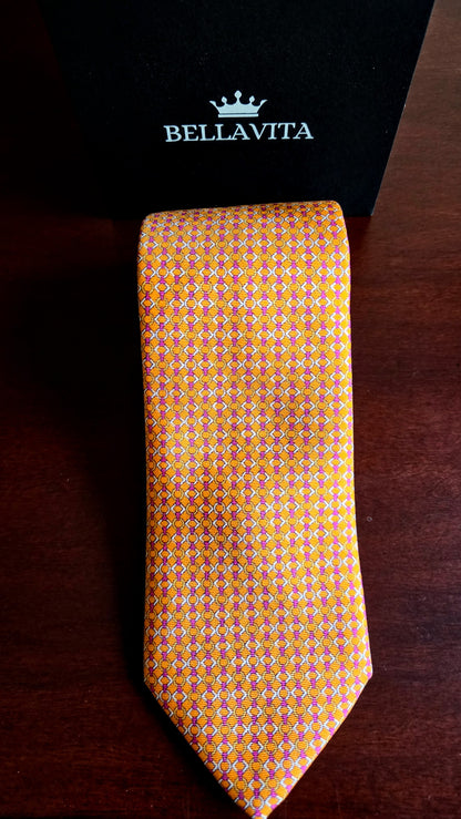 A Bellavita necktie with a yellow and orange geometric pattern, displayed vertically next to its black branded box on a dark wooden surface.