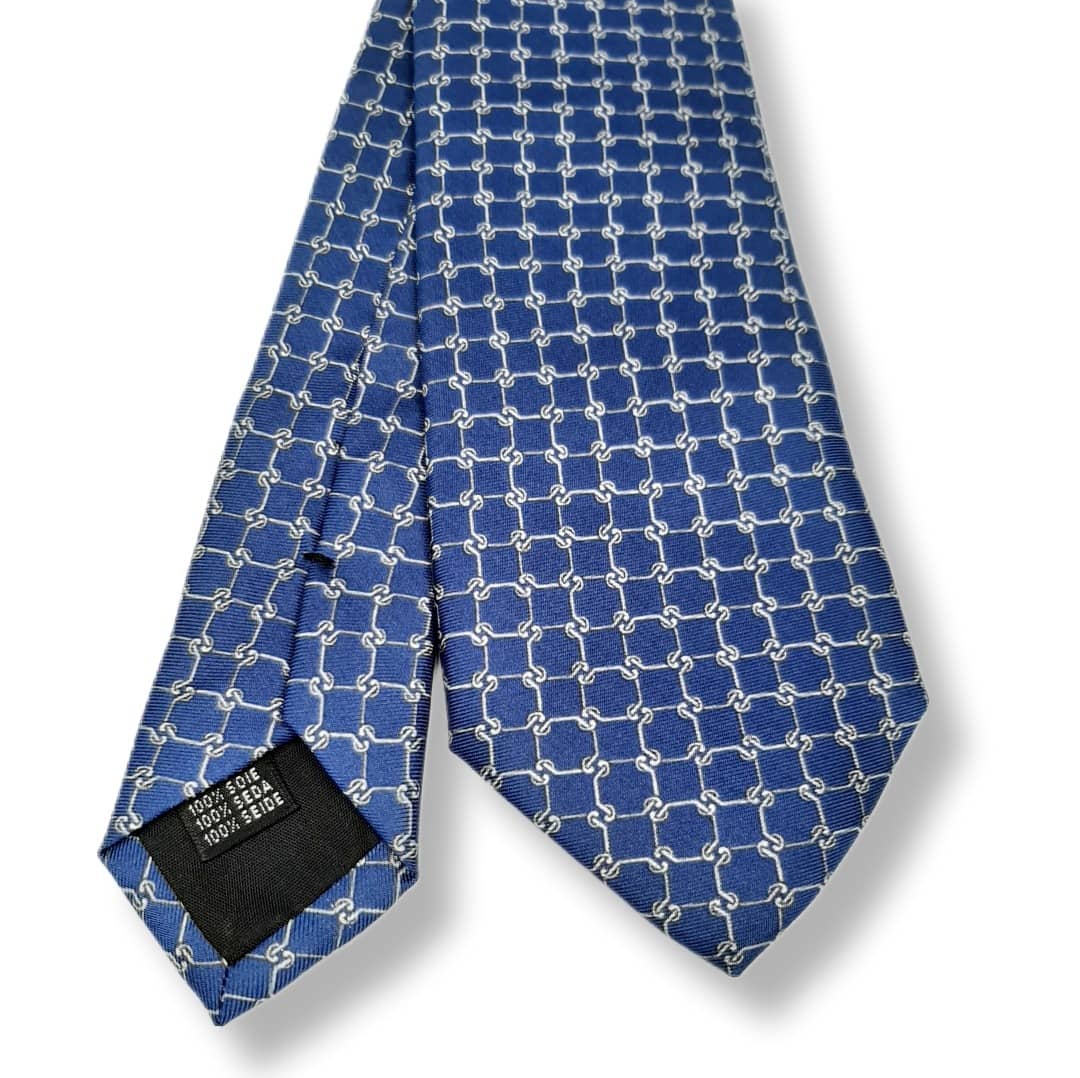 A blue silk necktie with a repeating white geometric interlocking-link pattern, shown folded on a white background with a black size label visible at the tip.