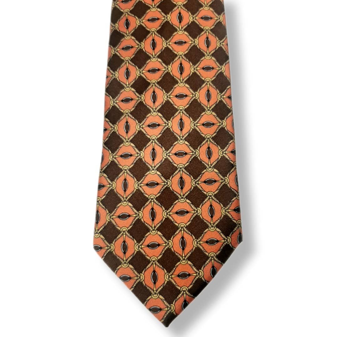 A necktie with a repeating geometric pattern of orange and brown diamonds outlined in gold, set against a dark brown background.