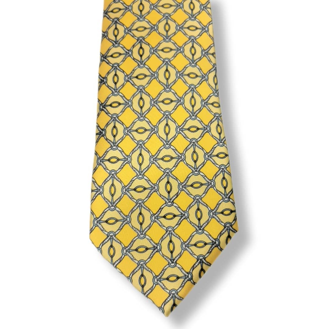 A yellow necktie with a repeating geometric pattern of interlocking diamond and oval motifs outlined in dark gray and black, shown against a plain white background.
