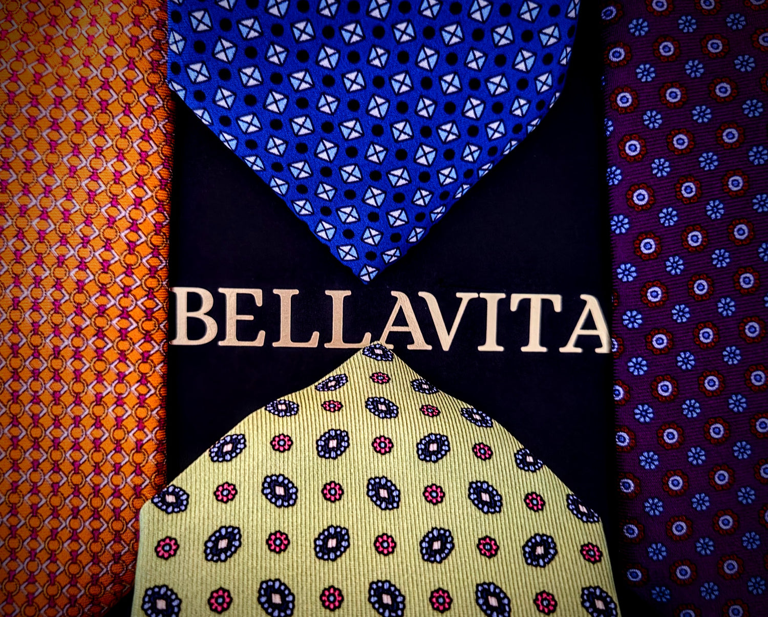 Four Bellavita neckties arranged vertically with the brand name 'BELLAVITA' centered over them. The ties feature distinct patterns: orange and red geometric, royal blue with white geometric, deep purple with blue geometric, and pale yellow with red and blue paisley.