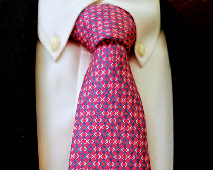 A red and blue patterned necktie knotted on a white dress shirt, displayed against a black background.